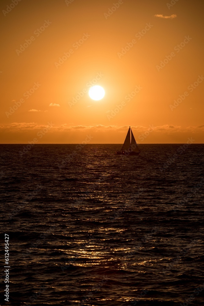 Vertical shot of a sunset on the seashore with a sailboat floating in the distance