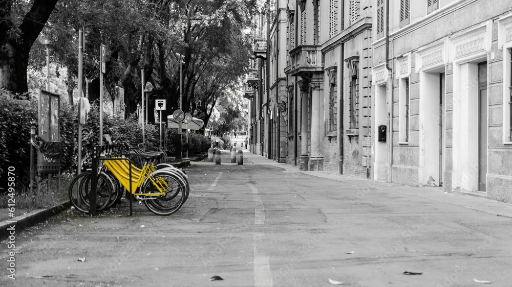 Fototapeta premium Greyscale of a narrow street in a town with bright yellow renting parked bikes