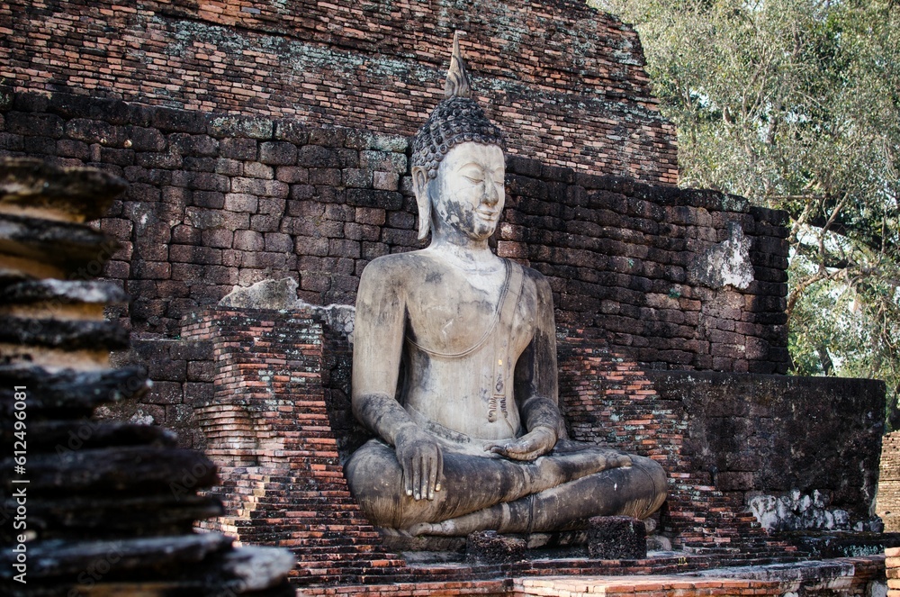 Fototapeta premium Sitting Buddha in Sukhothai, Thailand against a crumbled brick structure