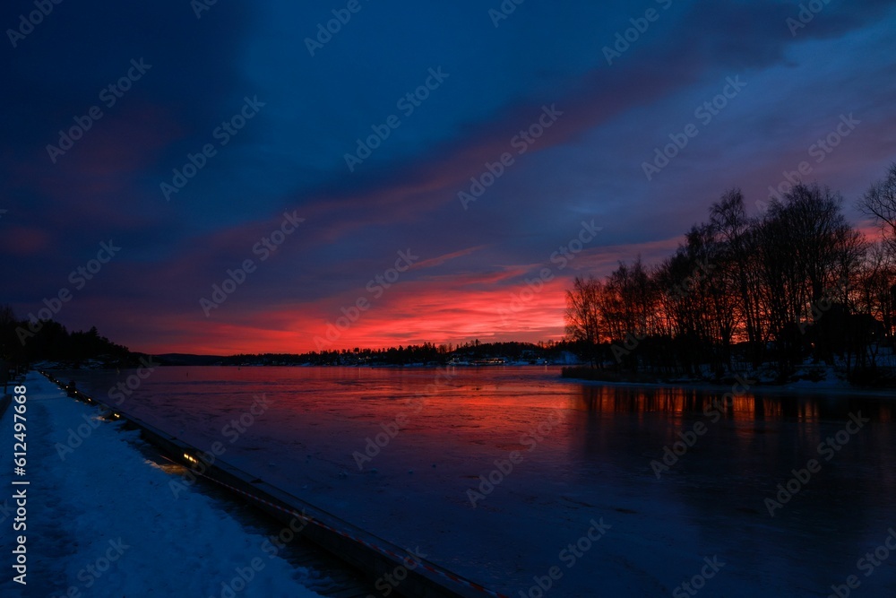 Mesmerizing evening scenery with a blue and red cloudy sky over the silhouette of trees by a lake