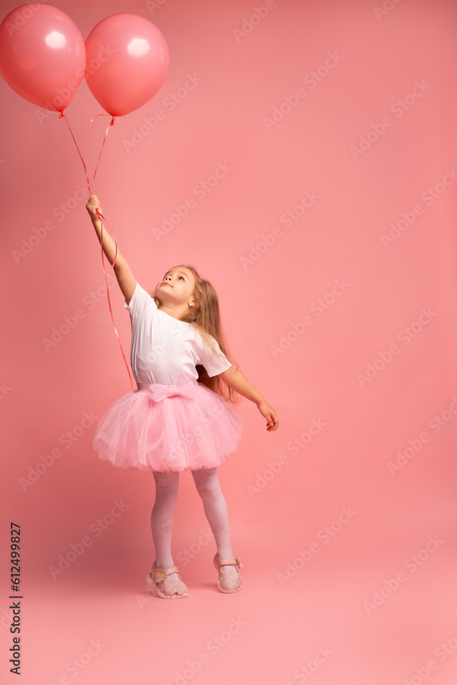 little girl in a white t-shirt and a pink tutu with balloons on pink background. Ready to fly high