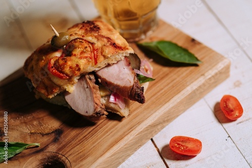 Freshly made sandwich is displayed on a wooden cutting board, with a chilled glass of beer