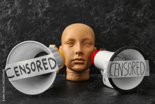 Taped megaphones with word CENSORED and human head on dark table photo