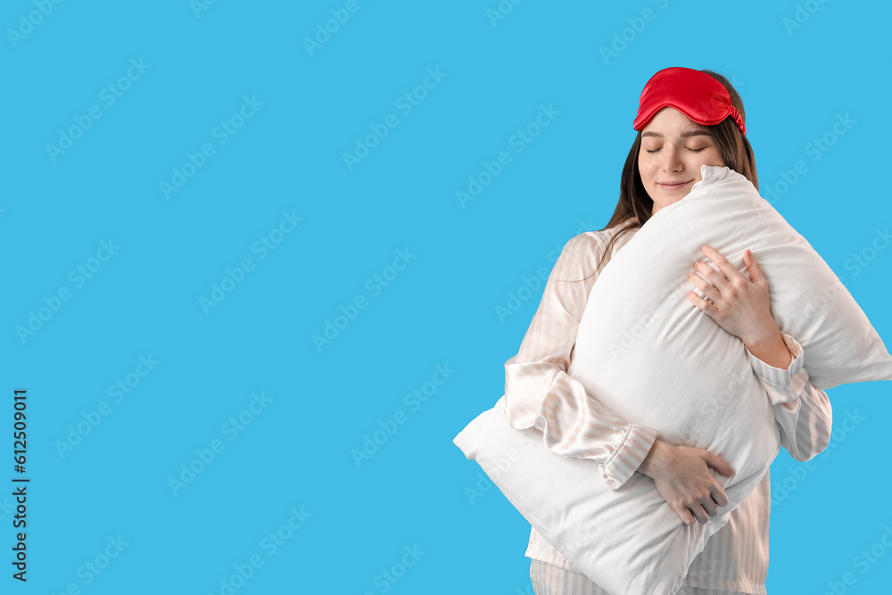 Young woman with sleeping mask and soft pillow on blue background Young woman with sleeping mask and soft pillow on blue background