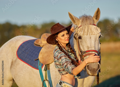 Happy young woman cowgirl in hat standing and hugging her horse photo