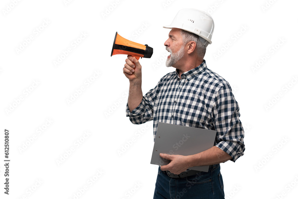 Builder shouts into megaphone. Mature man builder is holding megaphone. Blank for your building advertising. Copy space on gray. Message from construction company concept Builder shouts into megaphone. Mature man builder is holding megaphone. Blank for your building advertising. Copy space on gray. Message from construction company concept