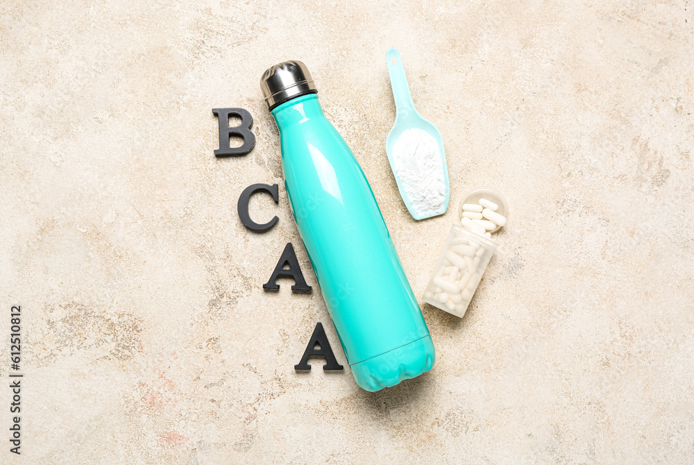 Letters BCAA, bottle of water, amino acid pills and powder on grunge background Letters BCAA, bottle of water, amino acid pills and powder on grunge background