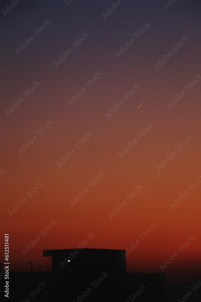 Silhouette houses in a distance under orange evening sky, vertical shot