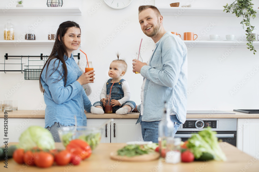 Front view of family trio making healthy meal in kitchen on sunday morning and posing with juice bottles. Happy people wearing denim attire smiling at camera. Concept of home fun and culinary. Front view of family trio making healthy meal in kitchen on sunday morning and posing with juice bottles. Happy people wearing denim attire smiling at camera. Concept of home fun and culinary.
