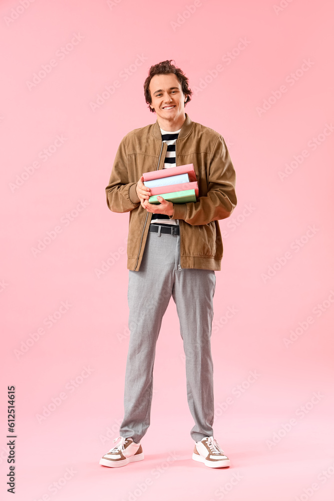 Young man with stack of books on pink background Young man with stack of books on pink background