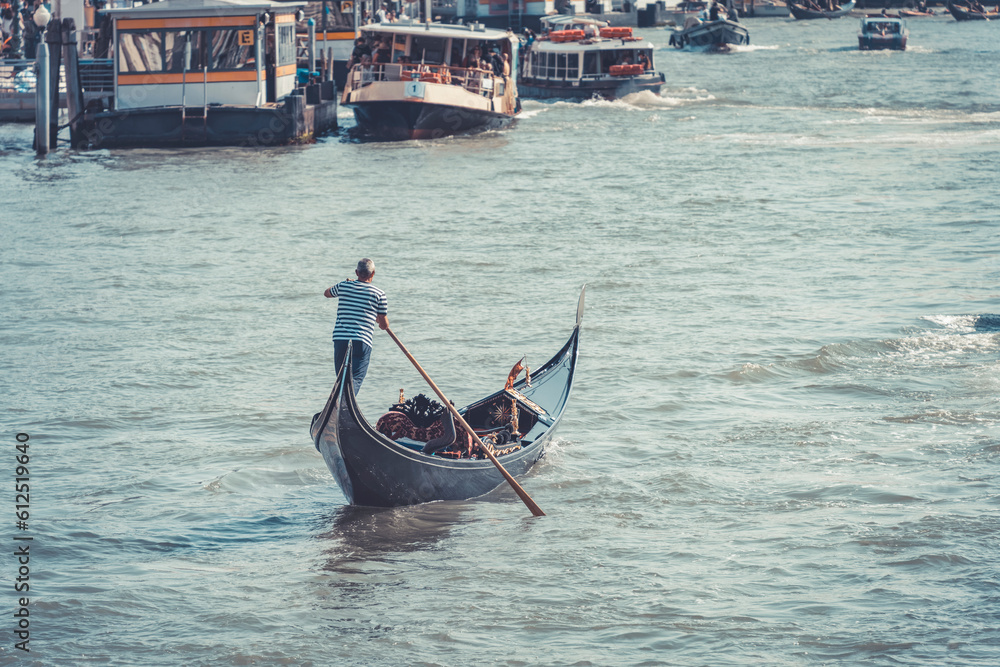 A gondolier or venetian boatman propelling a gondola on Grand Canal in Venice.