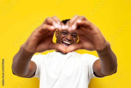 happy african american man in white t-shirt shows heart with his hands on yellow isolated background photo