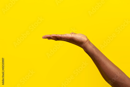 hand of african american man holds blank on yellow isolated background, guy asks and holds empty palm