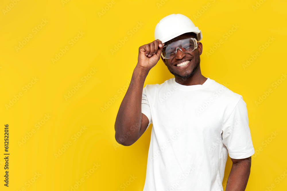 african american male civil engineer in hard hat and goggles smiles on yellow isolated background