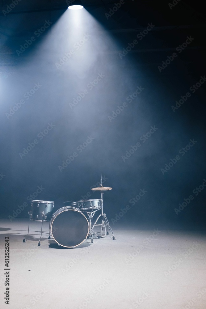 A drum set against a black background. A spotlight illuminates the drum from above and fog above