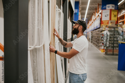 A young handsome man with a beard in casual clothes in a construction hypermarket in the lumber department selects wood building materials for the renovation of his house.