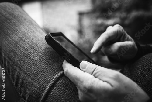 Close-up of person checking smartphone sitting on outdoor bench in a casual jean. Travel, connecting, relaxing, working, online, e-work, remort work concepts. Black and white retro photo.