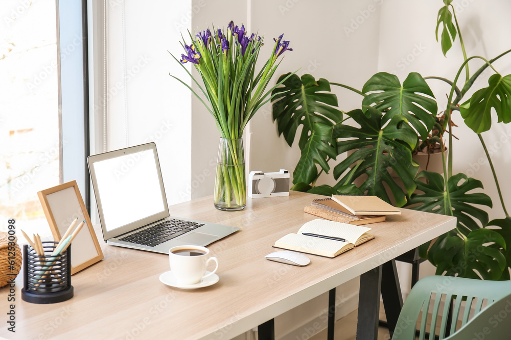 Modern workplace with laptop, notebooks, coffee cup and flowers in office Modern workplace with laptop, notebooks, coffee cup and flowers in office