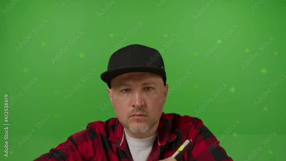 A caucasian man in black cap sitting before monitor and making notes and drawings on a green background A caucasian man in black cap sitting before monitor and making notes and drawings on a green background