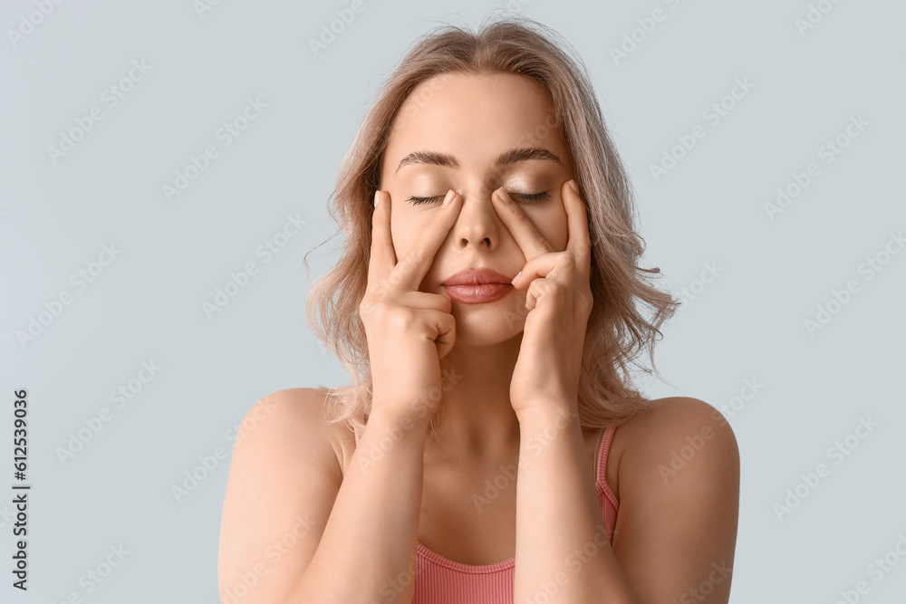 Young woman doing face building exercise on light background, closeup Young woman doing face building exercise on light background, closeup