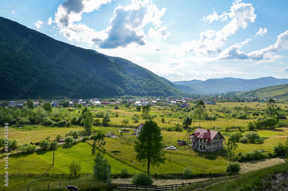 Beautiful landscape from a height. Typical Carpathian village in a valley, forest and mountains under blue sky with white clouds. Kolochava, Carpathians, Ukraine