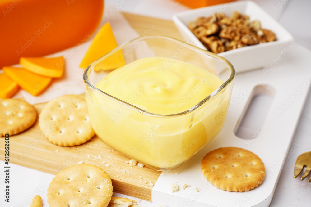 Bowls of tasty cheddar sauce with crackers, cheese chunks and walnuts on white grunge background Bowls of tasty cheddar sauce with crackers, cheese chunks and walnuts on white grunge background