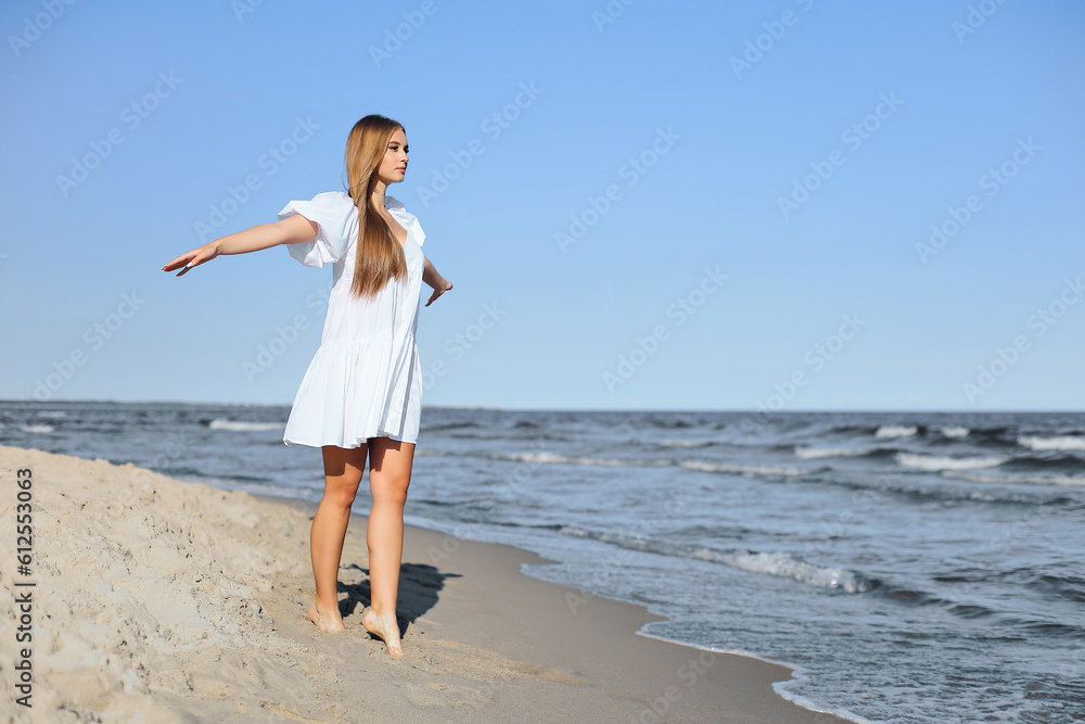 Happy smiling beautiful woman is walking on the ocean beach with open arms.