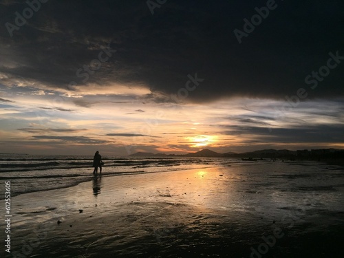 Silhouette shot of people walking on the shore of a beach during sunset