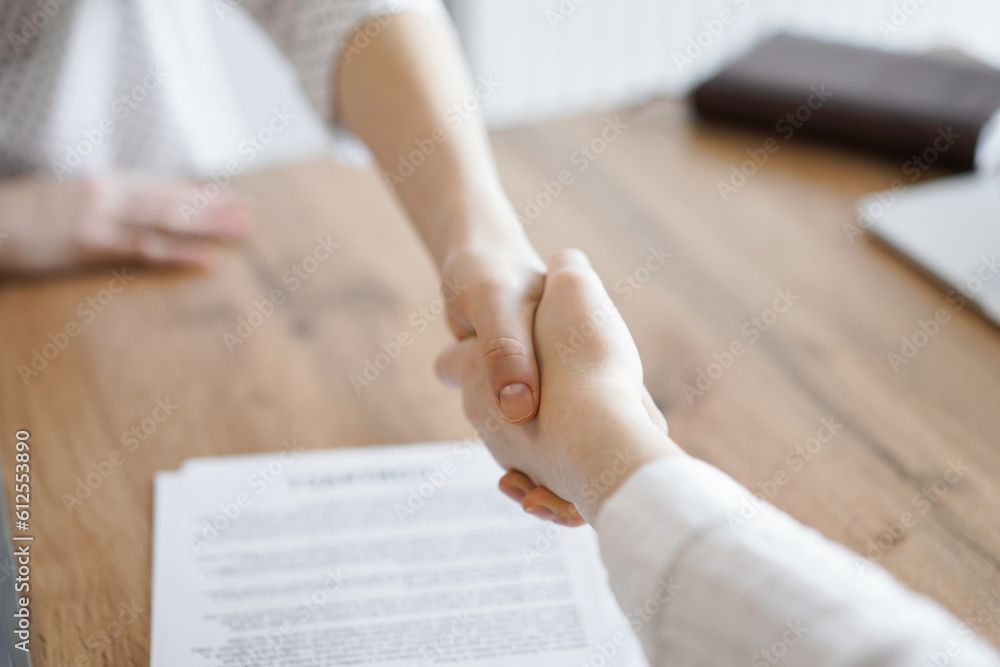 Obraz premium Business people shaking hands above contract papers just signed on the wooden table, close up. Lawyers at meeting. Teamwork, partnership, success concept.