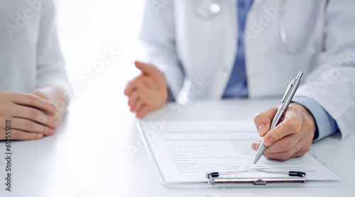 Doctor and patient discussing current health questions while sitting near of each other and using clipboard at the table in clinic, just hands closeup. Medicine concept.