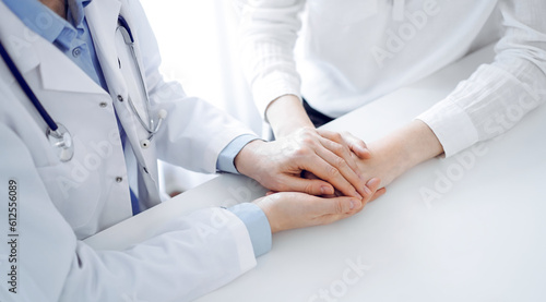 Doctor and patient sitting near each other at the table in clinic office. The focus is on female physician's hands reassuring woman, only hands, close up. Medicine concept.