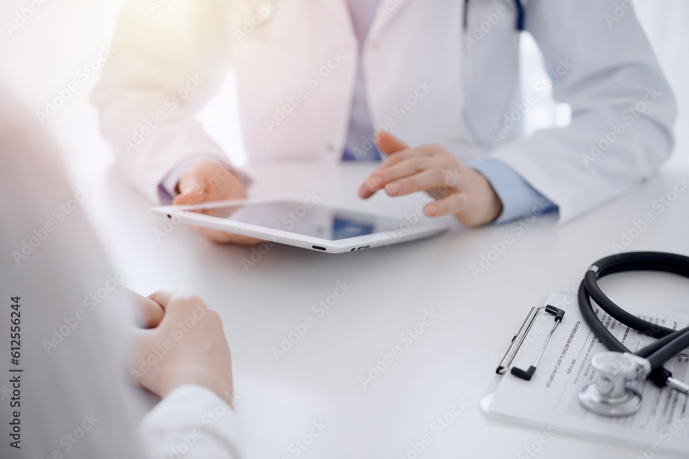 Stethoscope lying on the tablet computer in front of a doctor and patient sitting opposite each other and using tablet computer at the background . Medicine, healthcare concept. Stethoscope lying on the tablet computer in front of a doctor and patient sitting opposite each other and using tablet computer at the background . Medicine, healthcare concept.