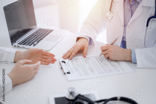 Doctor and patient discussing current health examination while sitting opposite each other at the desk in clinic. The focus is on female hands  close up. Medicine concept.