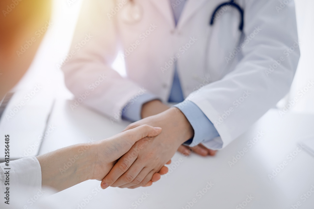Doctor and patient shaking hands while sitting opposite of each other at the table in clinic, just hands close up. Medicine concept. Doctor and patient shaking hands while sitting opposite of each other at the table in clinic, just hands close up. Medicine concept.