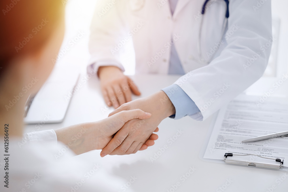 Doctor and patient shaking hands while sitting opposite of each other at the table in clinic, just hands close up. Medicine concept. Doctor and patient shaking hands while sitting opposite of each other at the table in clinic, just hands close up. Medicine concept.