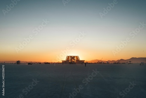 Distant shot of a building and people walking around it in a park during a golden sunset © Ben Gebo/Wirestock Creators