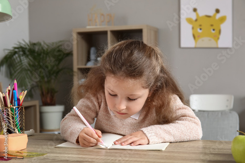 Cute little girl writing in copybook at home