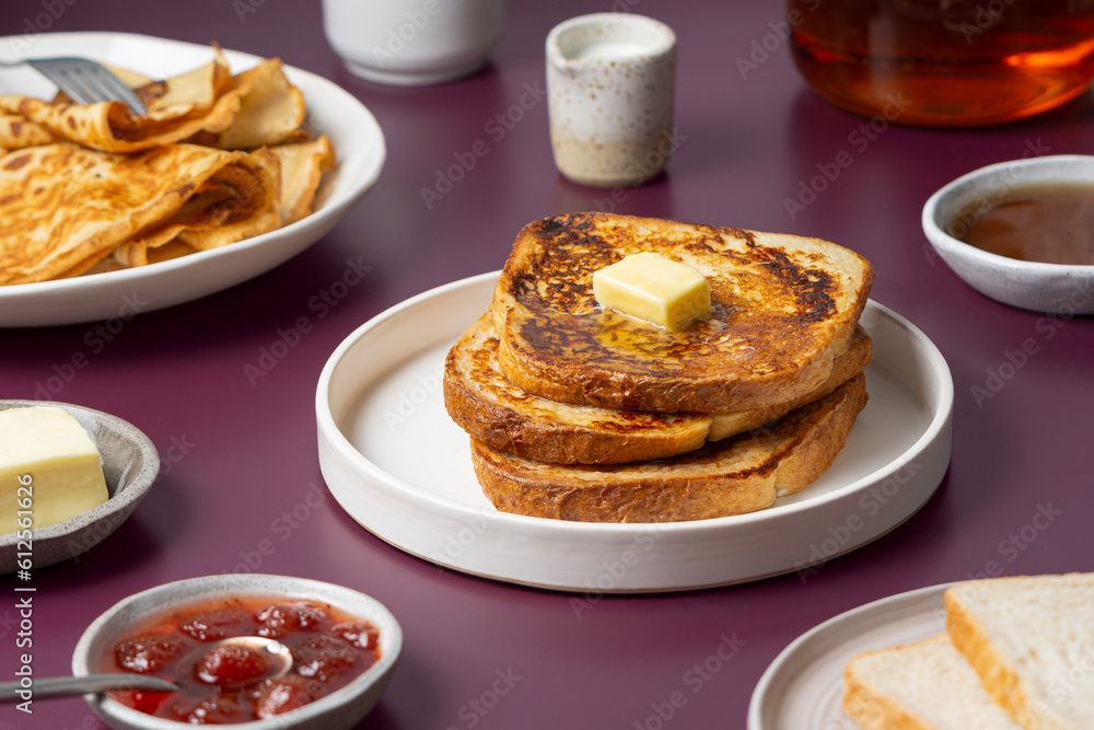 Morning meal - breakfast food. French toast with butter, pancakes, toast bread, jam, syrup, tea on a purple background. Morning meal - breakfast food. French toast with butter, pancakes, toast bread, jam, syrup, tea on a purple background.
