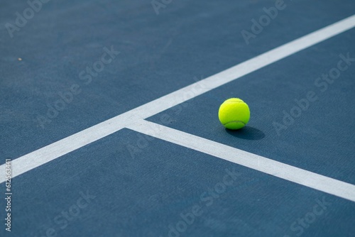 Landscape of a blue and green tennis court with a ball on it on a sunny day