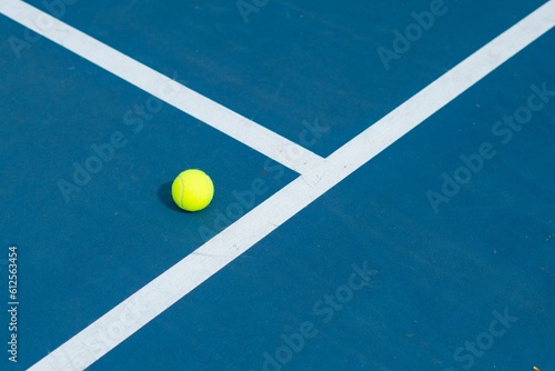 Landscape of a blue and green tennis court with a ball on it on a sunny day © Jwphotoworks/Wirestock Creators