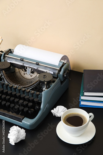 Vintage typewriter with cup of coffee and books on black table near beige wall