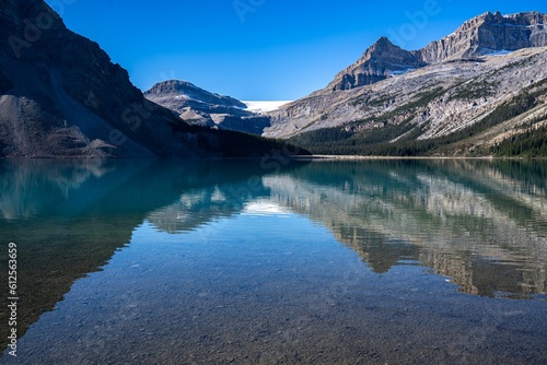 A transparent mountain lake's surface, with snowy mountain slopes in the background, on a sunny day