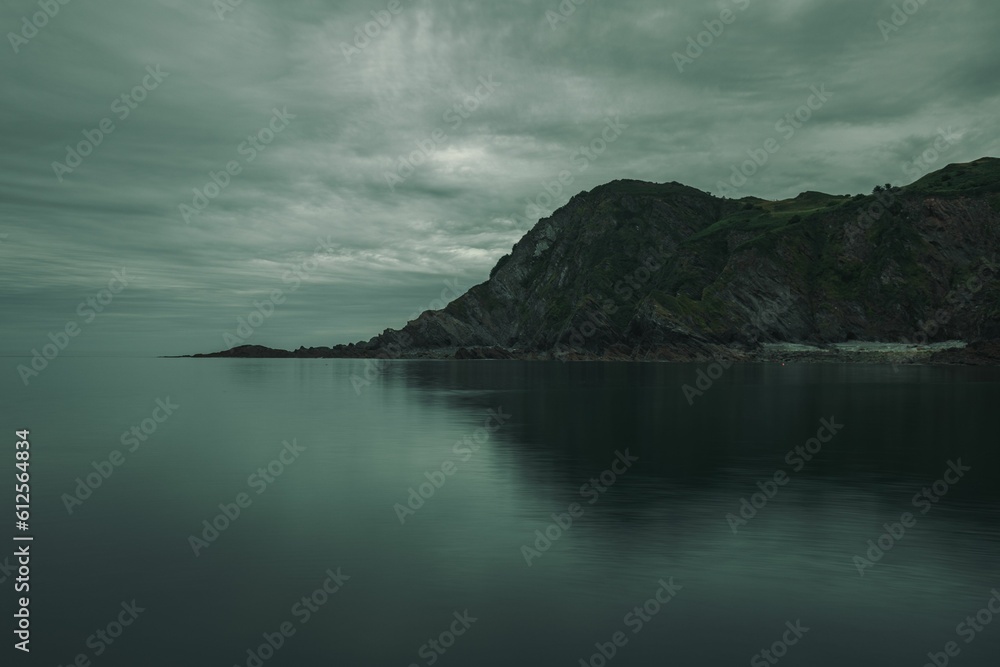 Mysterious gloomy landscape of the sea and rocky mountains in the background on a cloudy day