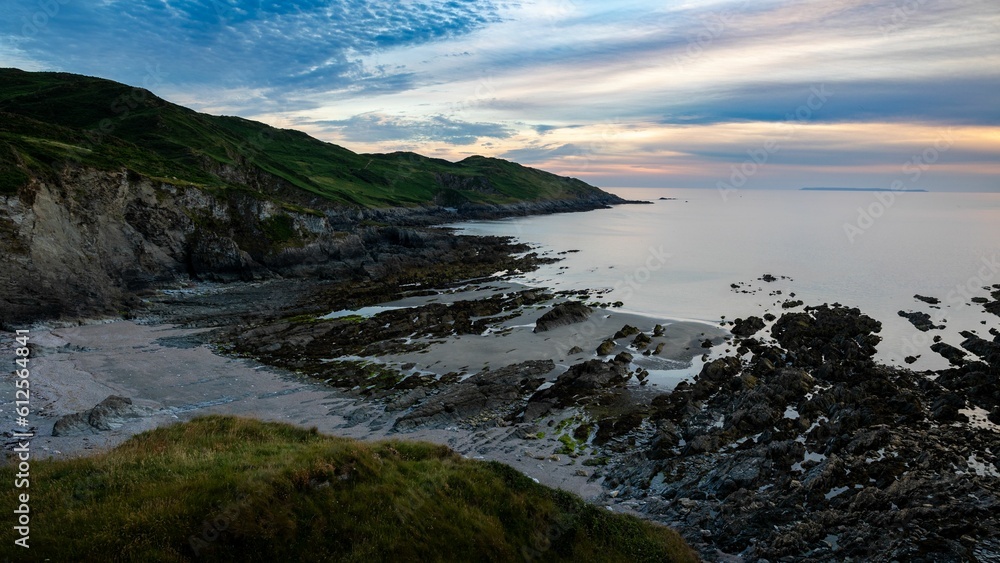 Fototapeta premium Scenic view of rocky beach and the sea under colorful cloudy sunset sky