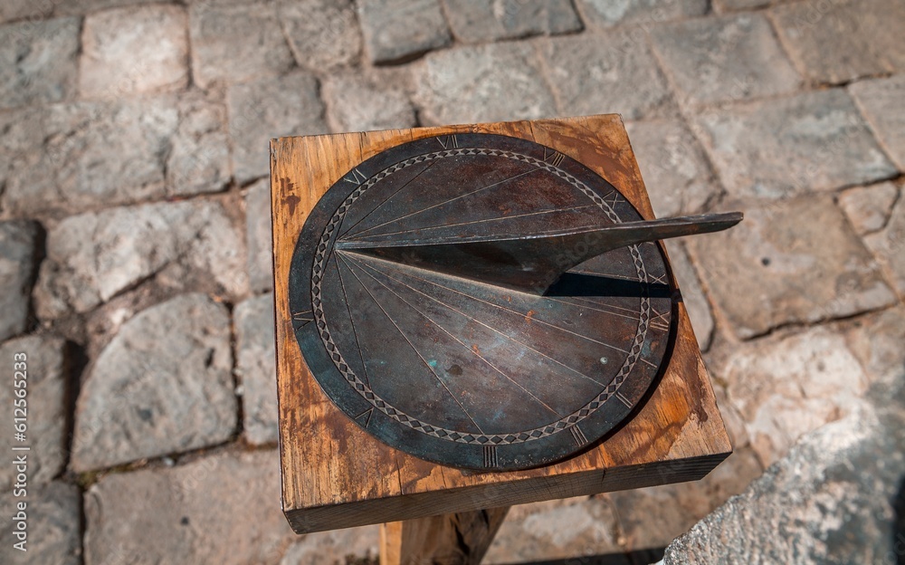 High-angle shot of an old sundial or a sun clock on the wooden surface on the blurred background