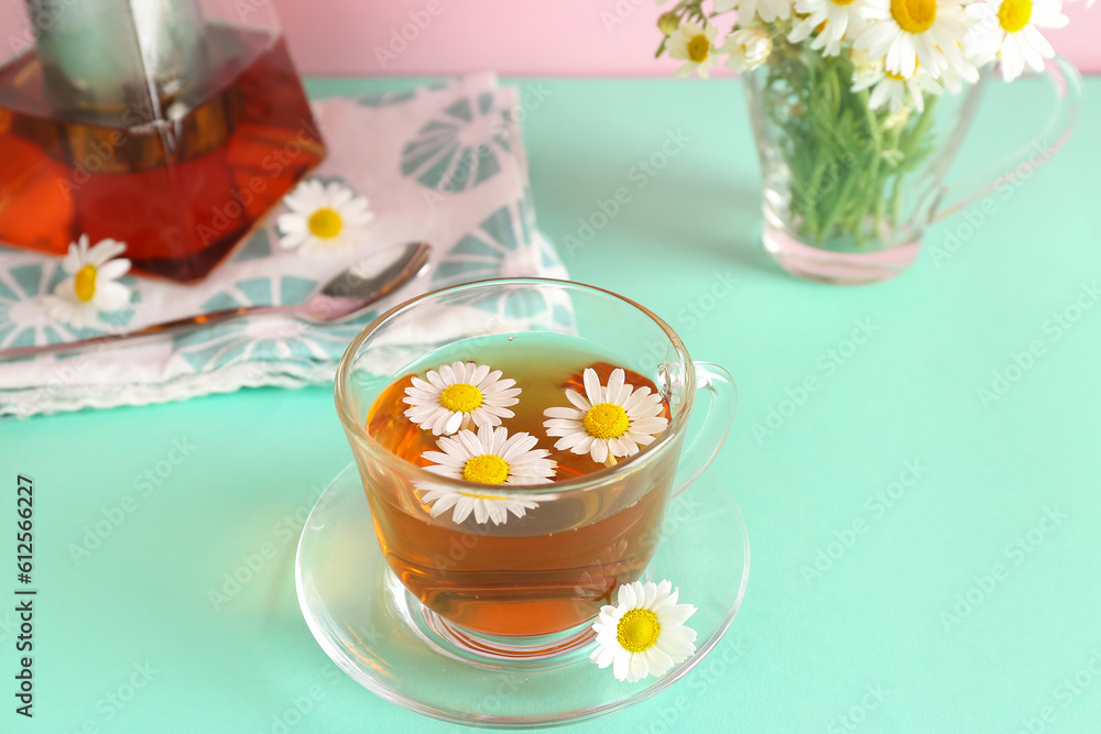 Teapot with cup of natural chamomile tea and flowers on turquoise table near pink wall Teapot with cup of natural chamomile tea and flowers on turquoise table near pink wall
