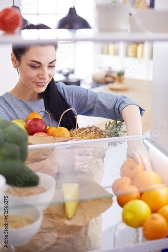 Smiling woman taking a fresh fruit out of the fridge, healthy food concept.