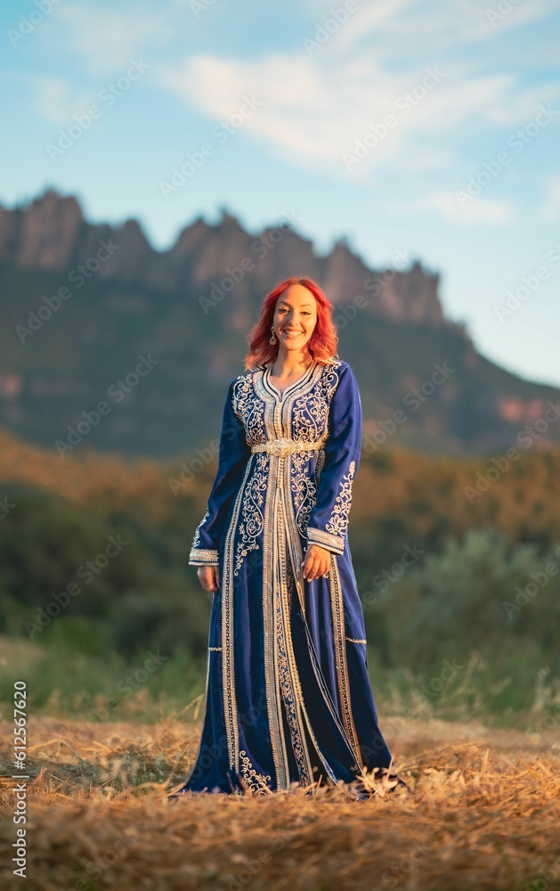 Beautiful smiling red-haired lady with a traditional blue dress decorated with goldwork in a field Beautiful smiling red-haired lady with a traditional blue dress decorated with goldwork in a field