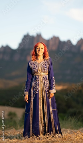 Beautiful red-haired woman in a traditional blue dress with goldwork ornamentations in a sunny field photo