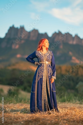 Beautiful red-haired lady with a traditional blue dress decorated with goldwork in a field